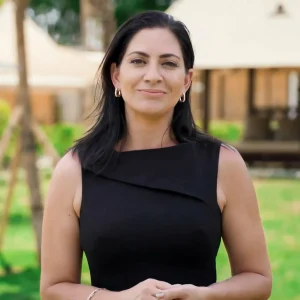 A woman in a sleeveless black dress smiling outdoors with a glamping tent in the background